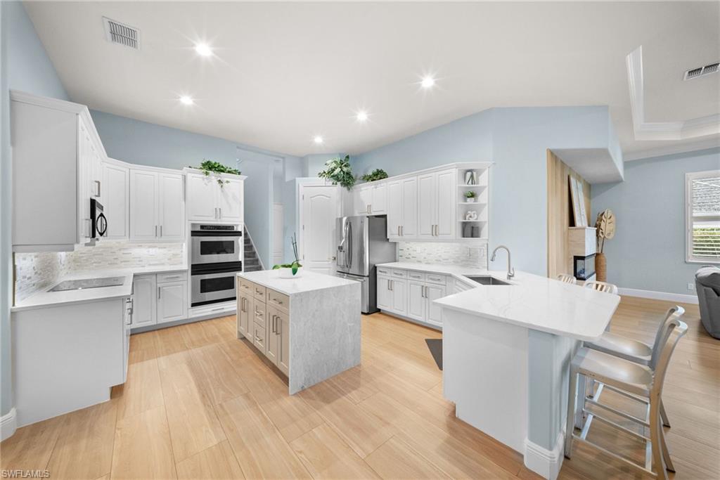 Spacious kitchen featuring light wood-finish flooring, white cabinetry, integrated stainless-steel appliances, and a central island with a waterfall countertop
