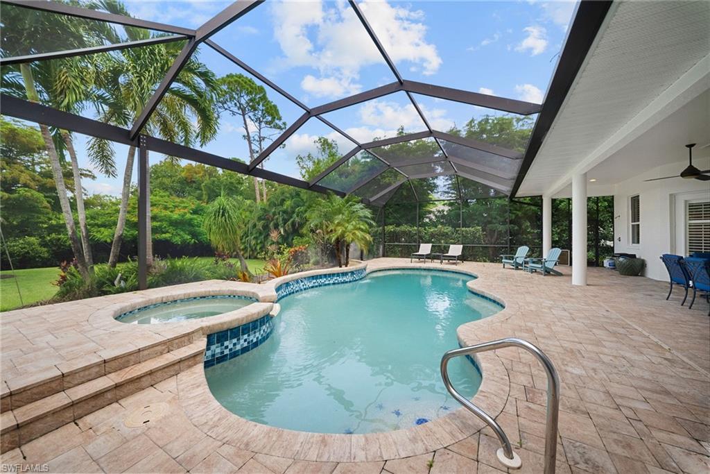 Screened lanai featuring a freeform pool, integrated spa, and extensive paver decking