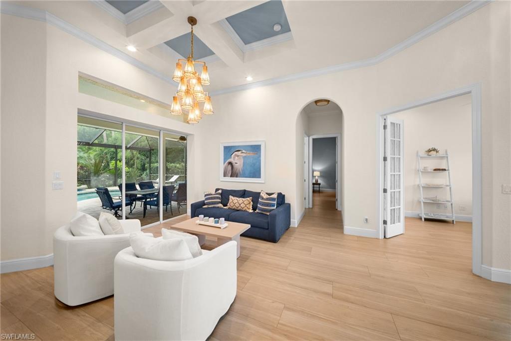 Living area featuring wood-finish flooring, a coffered ceiling with a chandelier, and sliding glass doors opening to a screened lanai with a pool