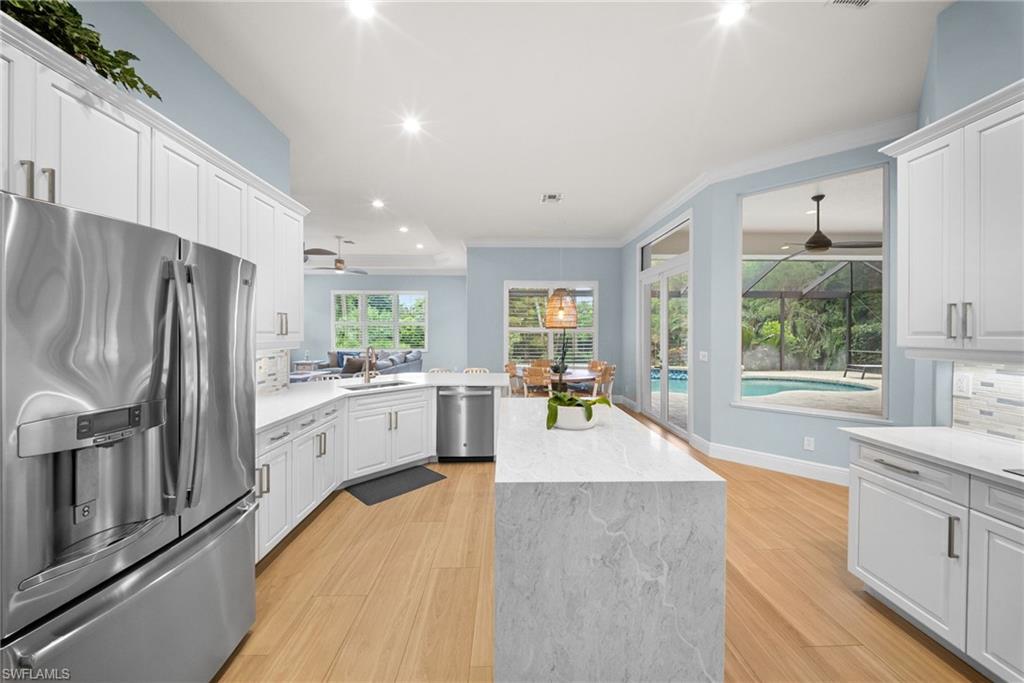 Open-concept kitchen featuring white shaker cabinetry, stainless steel appliances, wood-finish flooring, a large island with a stone countertop, and direct access to an outdoor pool area