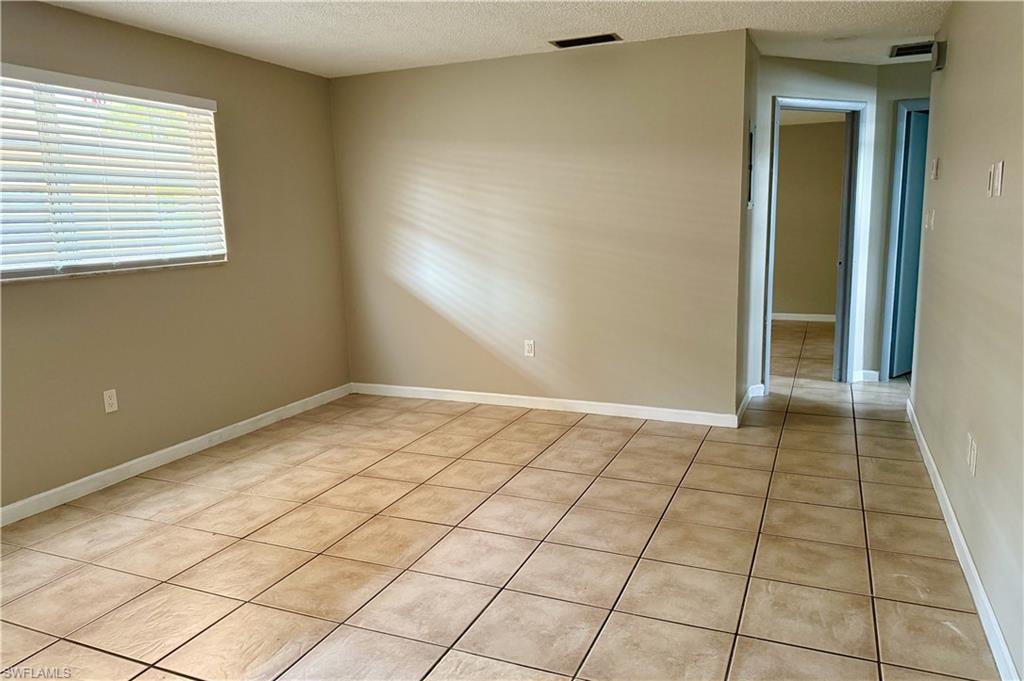 Spacious room featuring neutral-toned walls, tile flooring throughout, and abundant natural light from a large window with plantation shutters