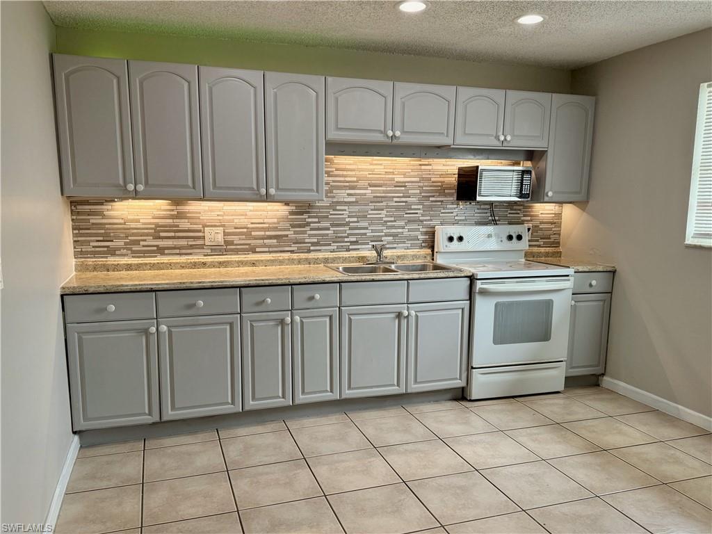 Kitchen featuring grey shaker-style cabinetry, granite-look countertops, and a mosaic tile backsplash