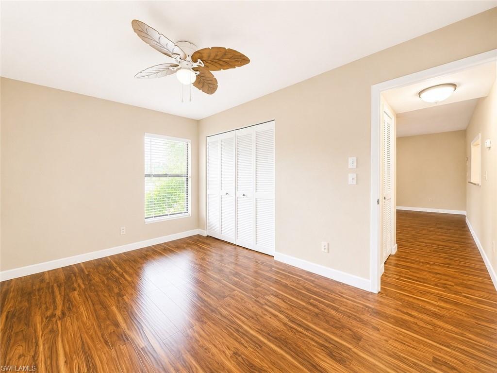 Spacious room featuring wood-finish flooring, neutral-toned walls, a window with blinds, bi-fold closet doors, and a decorative ceiling fan with integrated lighting