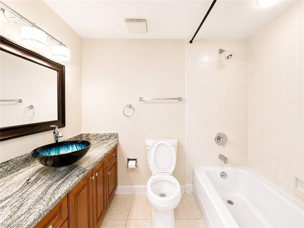 Bathroom featuring a vessel sink, wood-finish vanity, light-toned countertop, ceramic floor tile, and a tiled shower/tub combination