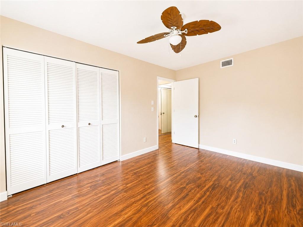 Spacious room featuring rich wood-finish flooring, louvered bi-fold closet doors, a ceiling fan with light fixture, and neutral wall tones