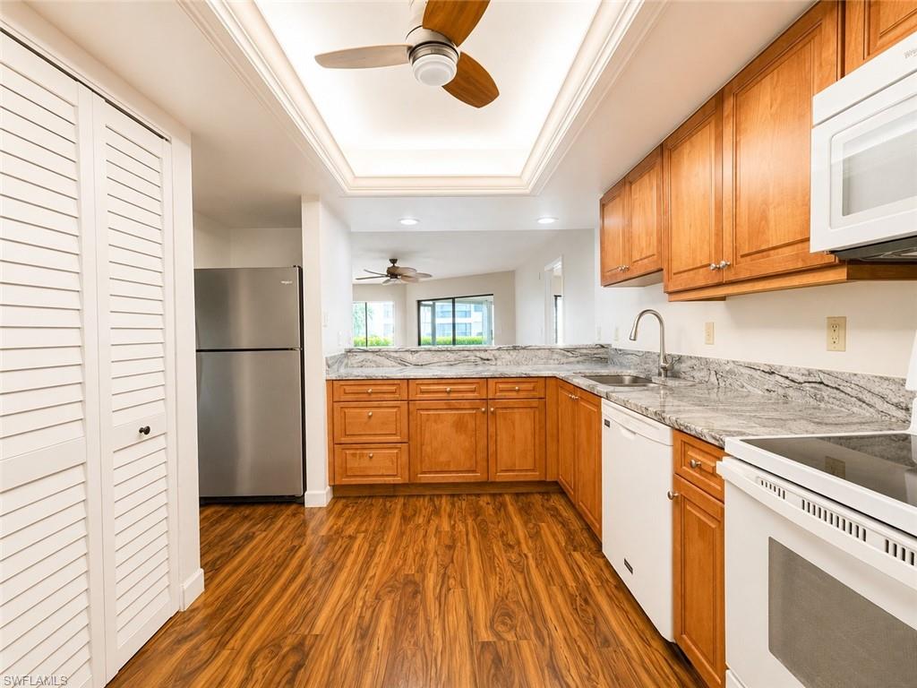Kitchen featuring wood-finish flooring, wood cabinetry, granite countertops, and a full suite of white appliances