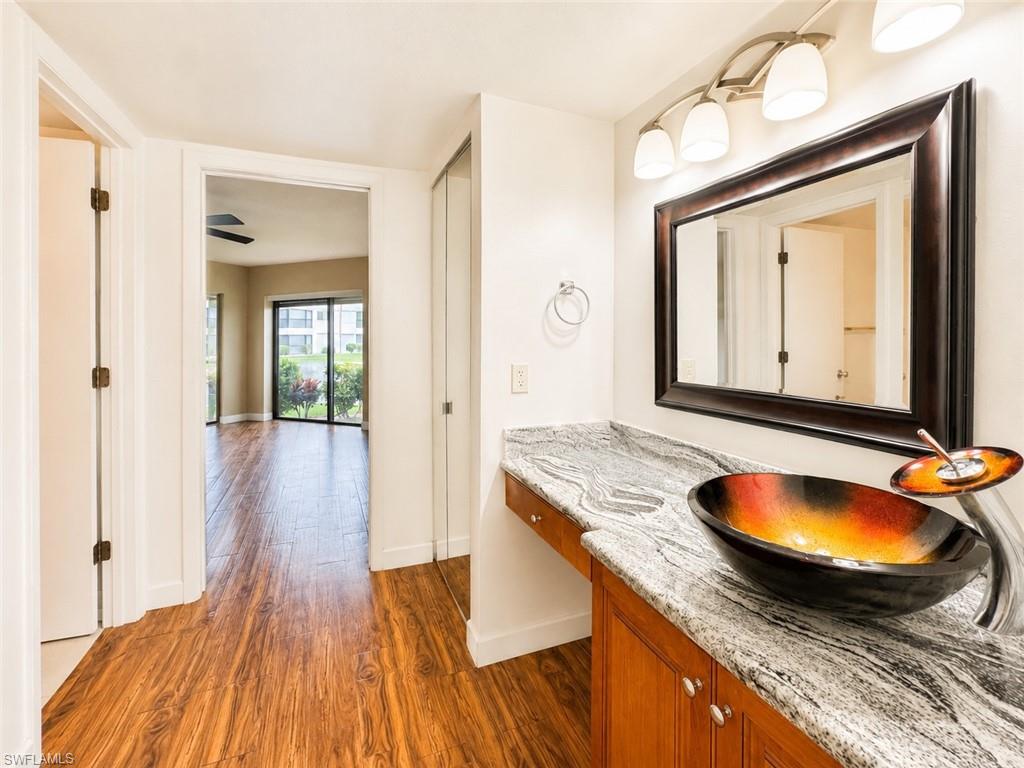 Vanity area featuring a vessel sink, stone countertop, wood-finish flooring, and a large framed mirror