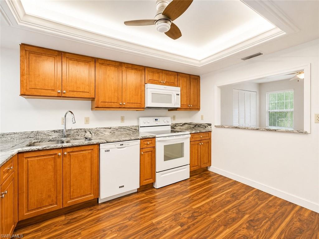 Kitchen featuring wood-finish flooring, light wood cabinetry, white appliances, and speckled countertops