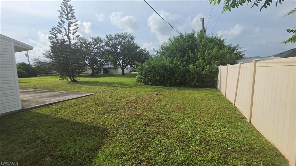 Expansive green lawn featuring a privacy fence, mature trees, and a concrete patio