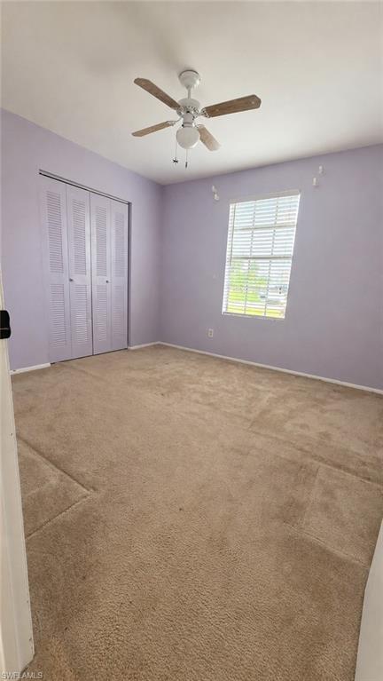 Carpeted room featuring a ceiling fan with light fixture, louvered bi-fold closet doors, and a window with horizontal blinds