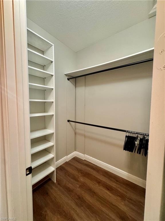 Walk-in closet featuring wood-finish flooring, white built-in shelving, and two clothing rods