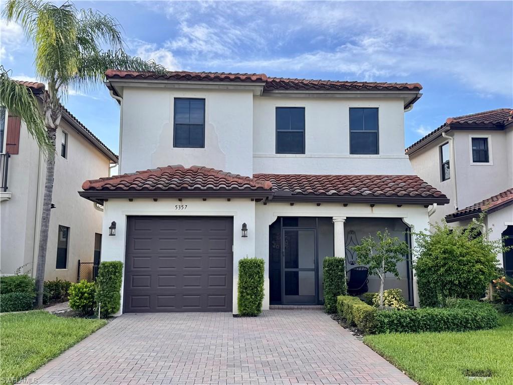 Mediterranean-style home featuring a red tile roof, stucco exterior, screened-in porch, paver driveway, and an integrated garage