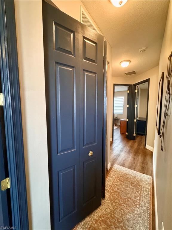 Hallway with wood-finish flooring, recessed lighting, and a dark-paneled bifold door featuring decorative hardware