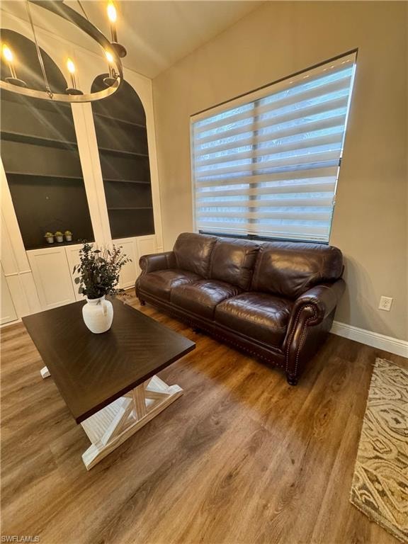 Wood-finish flooring throughout, featuring a window with banded shades, built-in shelving with arched accents, and recessed lighting