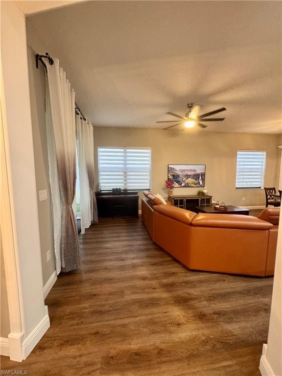 Open-concept living area featuring wood-finish flooring, a ceiling fan with integrated lighting, and multiple windows with horizontal blinds