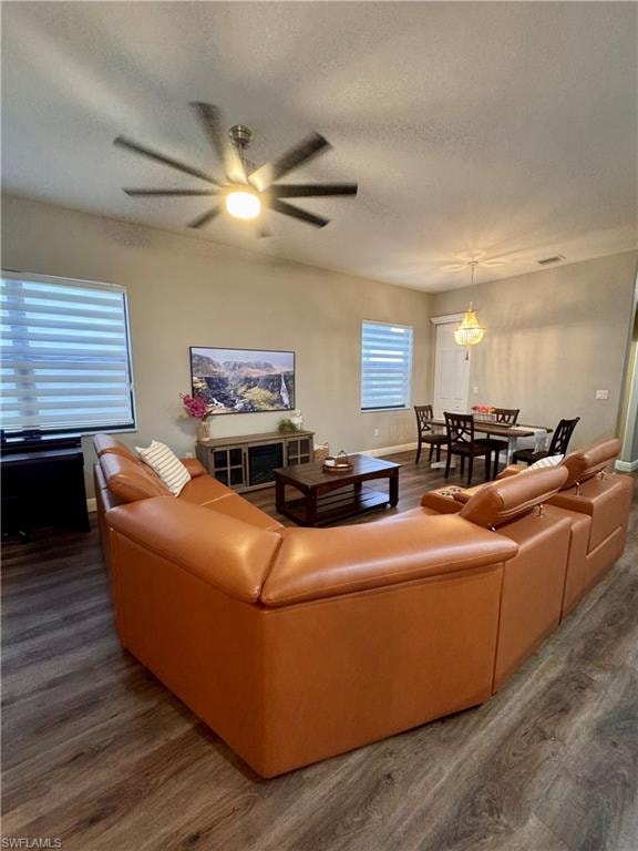 Open-concept living space featuring wood-finish flooring, a contemporary ceiling fan, and multiple windows with horizontal blinds