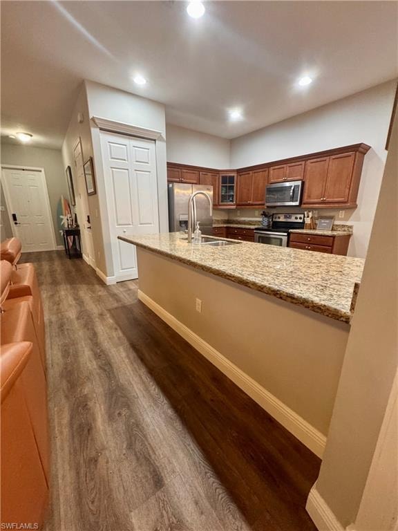 Modern kitchen featuring an island with a built-in sink, granite countertops, wood-finish flooring, recessed lighting, and stainless steel appliances