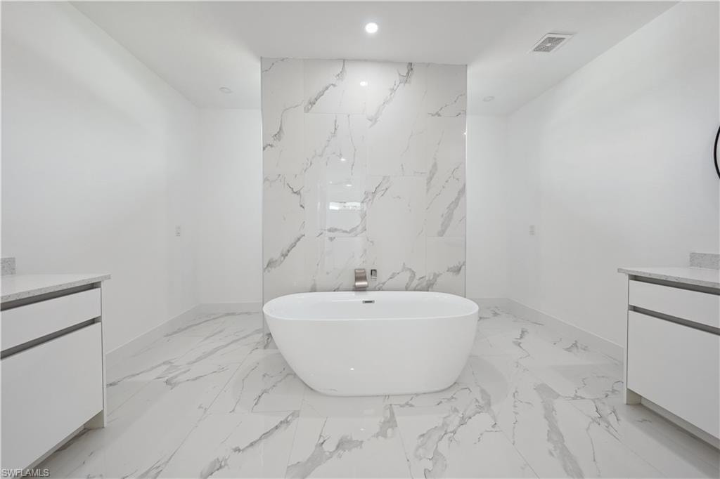Freestanding soaking tub with a wall-mounted faucet, complemented by large format marbled-finish floor and wall tiles