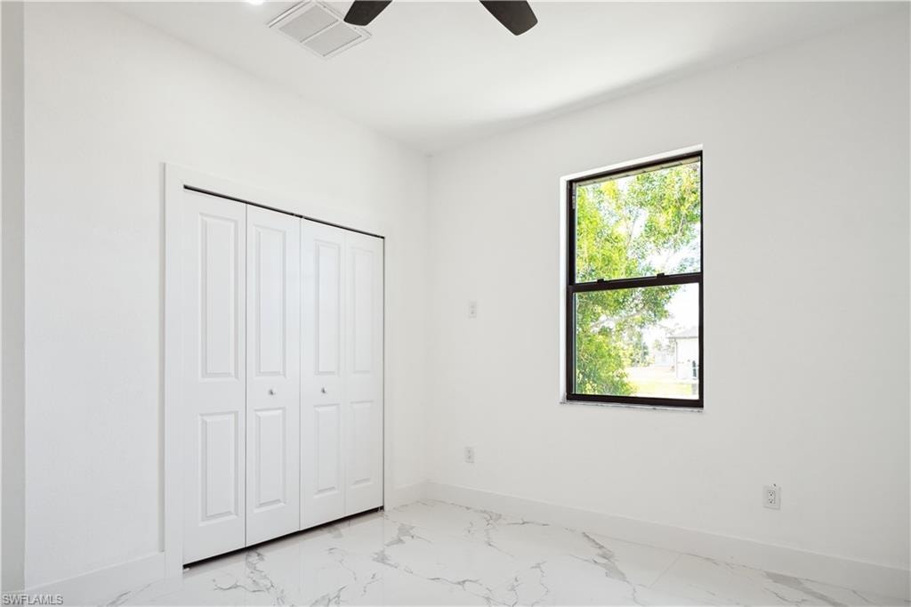 Room featuring a single window with a black frame, white walls, and large format white tile flooring with gray veining