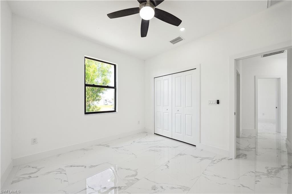 Room featuring white walls, marble-finish flooring, a ceiling fan with integrated lighting, a bi-fold closet, and a single window with black trim