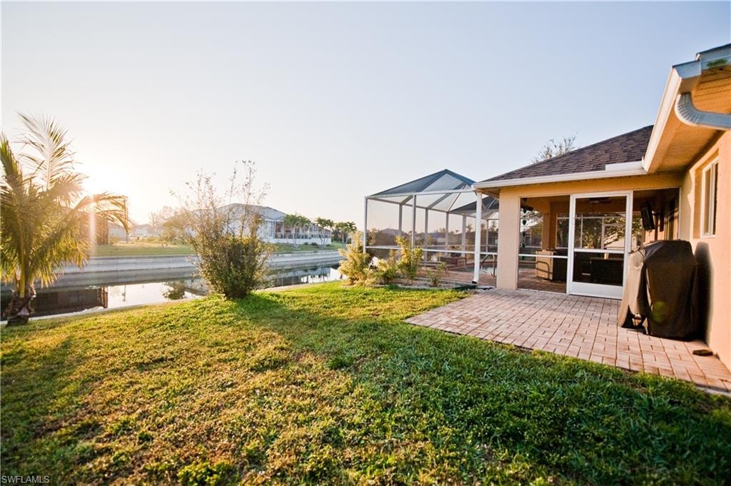 Expansive green lawn bordering a canal, featuring a screened lanai with a patio, and a covered outdoor living area
