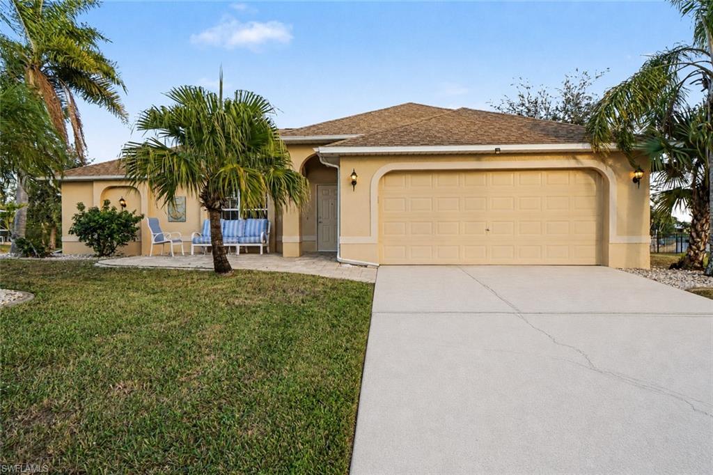Single-story stucco residence featuring an attached garage, paved driveway, and mature landscaping