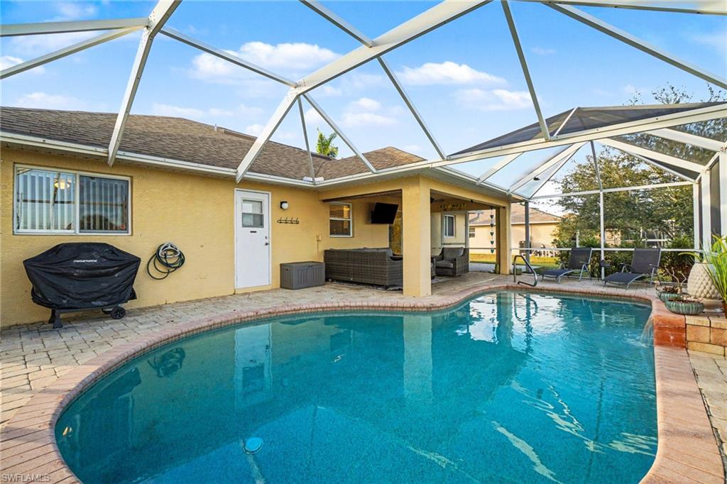 Screened-in outdoor living space featuring a free-form swimming pool with brick paver surround, covered patio area, and exterior access door