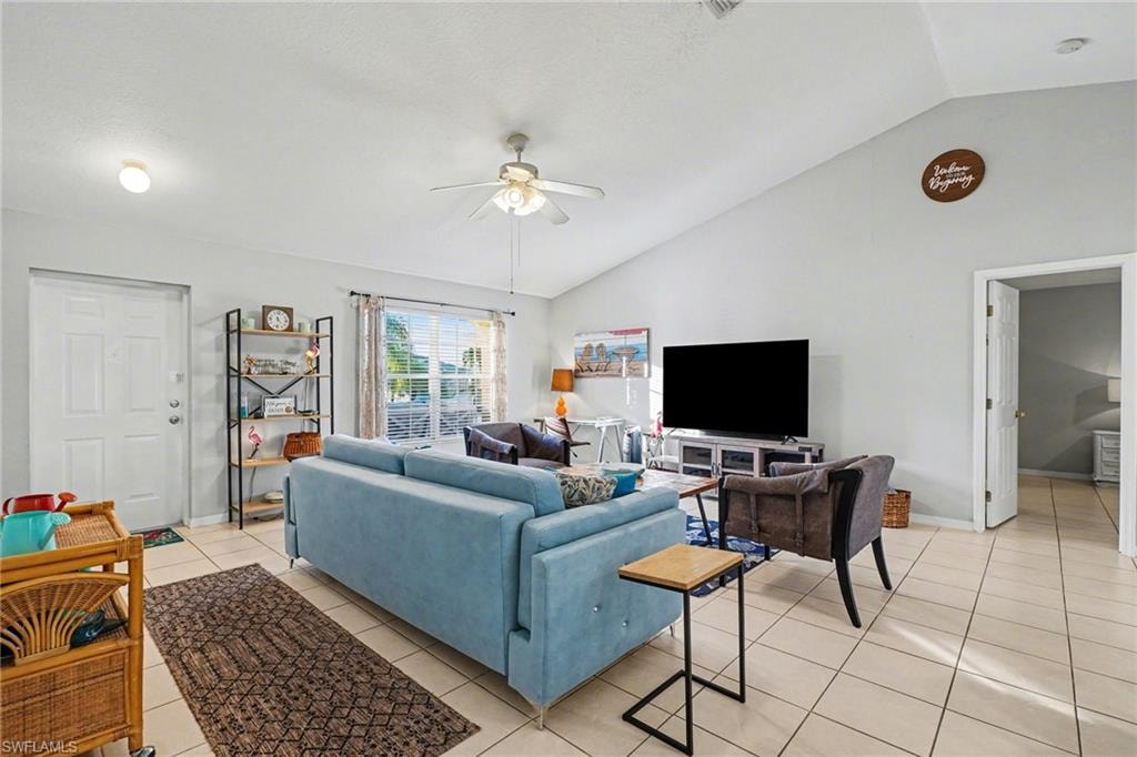 Living room featuring vaulted ceilings, neutral wall tones, ceramic tile flooring, a ceiling fan with integrated lighting, and a large window providing natural illumination