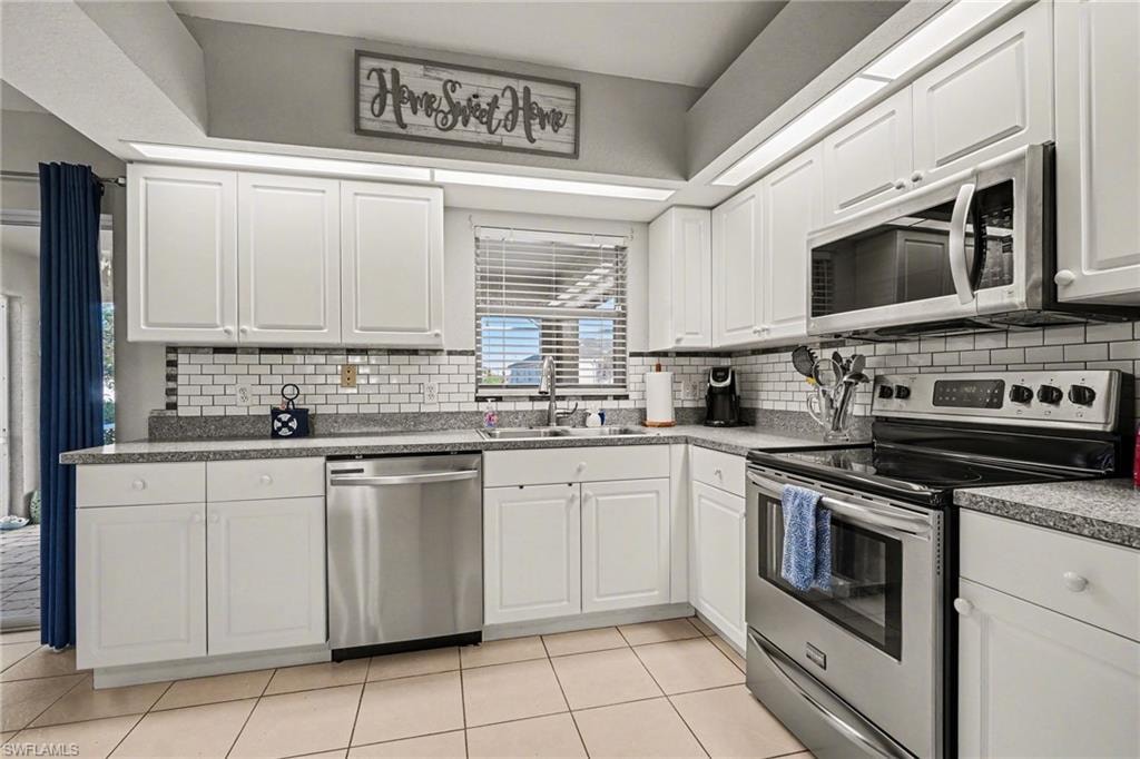 Bright kitchen with white cabinetry, stainless steel appliances, speckled countertops, and a white subway tile backsplash