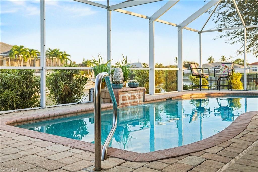 Screened lanai featuring a swimming pool with a waterfall feature, brick paver decking, and a stainless steel grab rail
