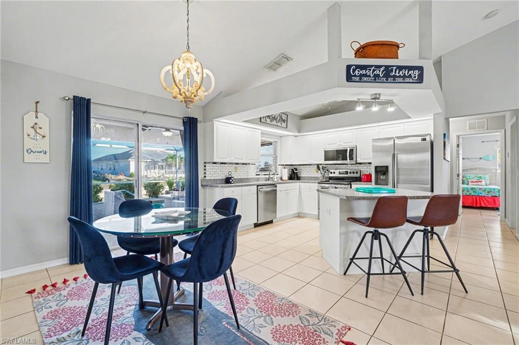 Open-concept kitchen and dining area featuring white cabinetry, stainless steel appliances, a kitchen island with seating, a glass dining table, and direct outdoor access via sliding glass doors