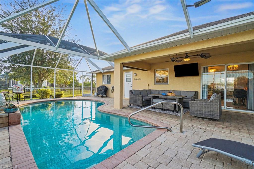 Screened lanai featuring a free-form swimming pool with brick paver surround, a covered patio area with an integrated ceiling fan, and sliding glass doors providing interior access