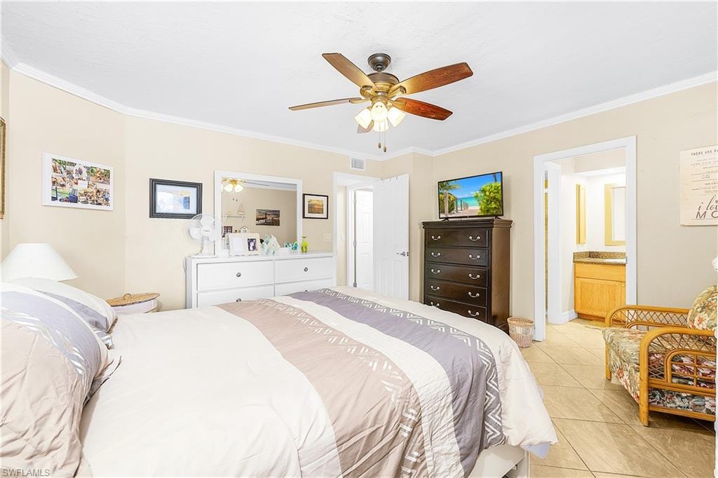 Well-appointed room featuring crown molding, a ceiling fan with light fixture, tile flooring, and a doorway revealing a vanity with a countertop and mirror