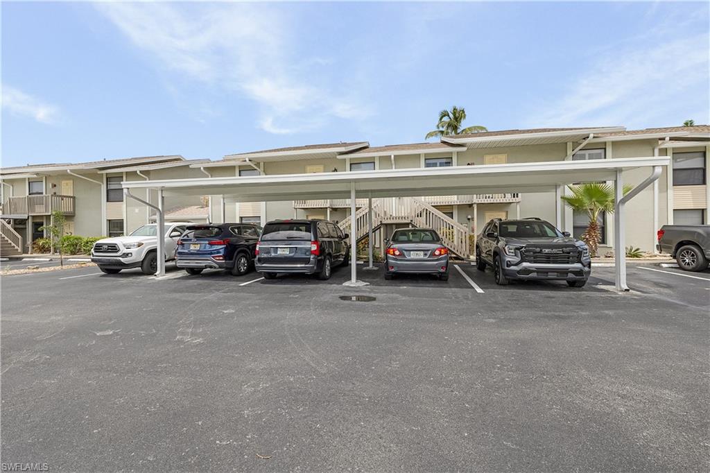 Asphalt parking lot featuring a white metal carport structure providing covered parking