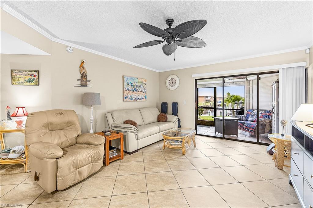 Spacious living area featuring neutral-toned tile flooring, crown molding, and a ceiling fan