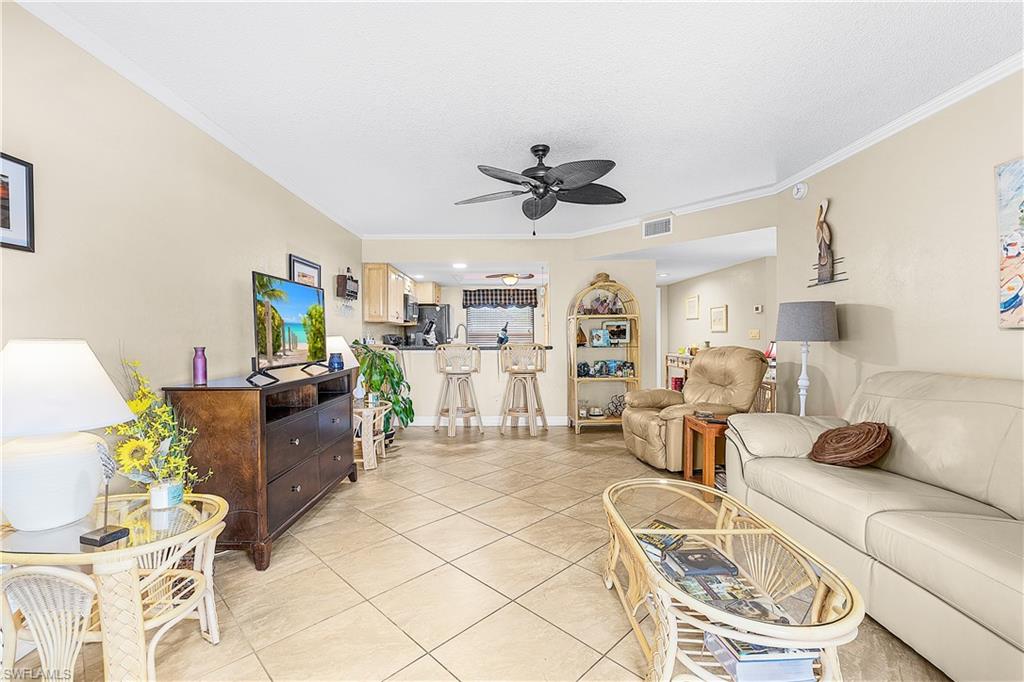 Open concept living area featuring tile flooring, crown molding, a ceiling fan, and an integrated kitchen with a breakfast bar