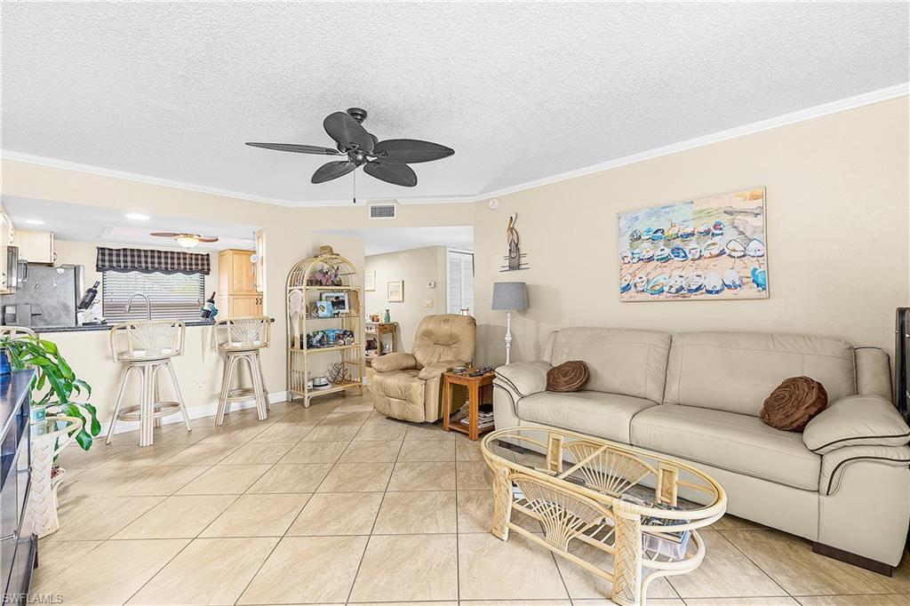 Open concept living area featuring light-toned tile flooring, recessed lighting, and crown molding
