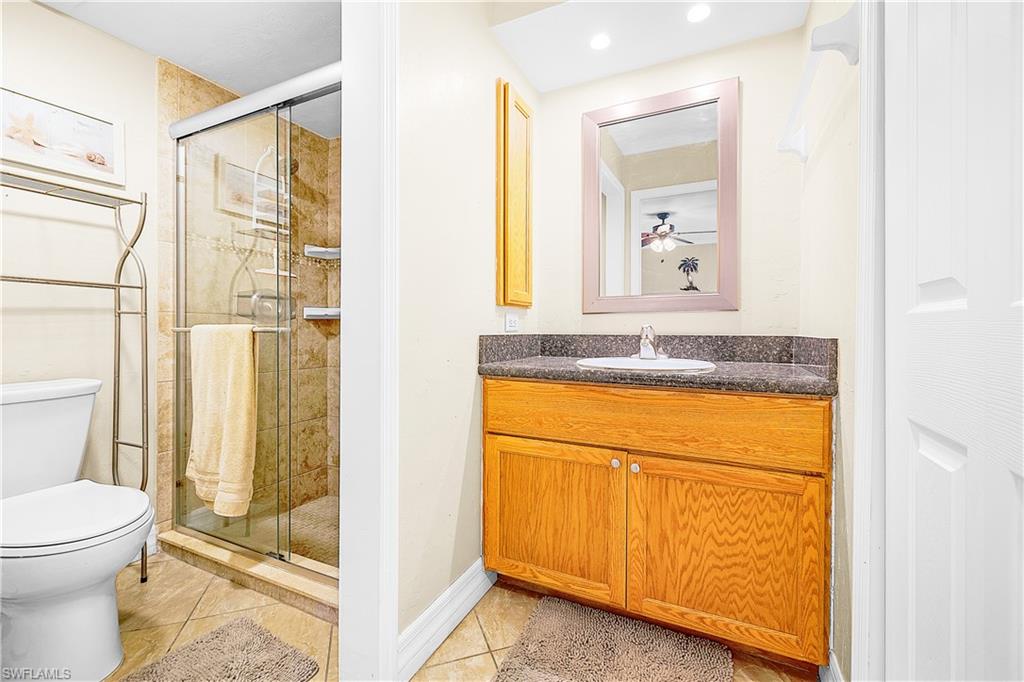 Bathroom featuring a wood-finish vanity with a dark countertop and undermount sink, a framed wall mirror, a glass-enclosed shower with tiled walls, and ceramic tile flooring