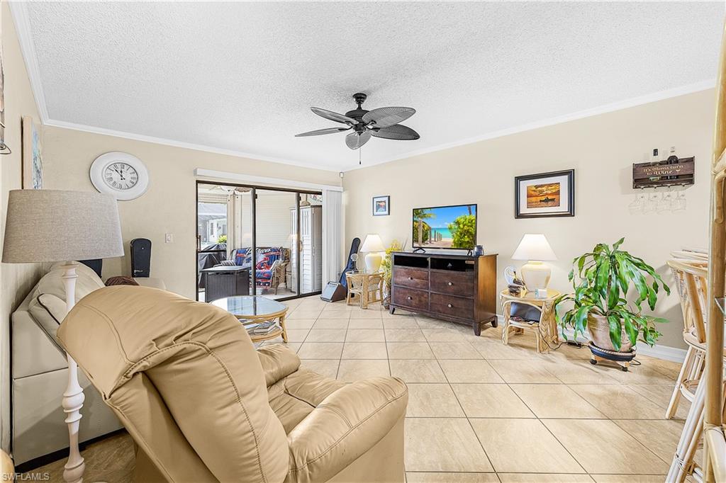 Living area featuring tile flooring, crown molding, a ceiling fan with light, and sliding glass doors opening to an enclosed patio