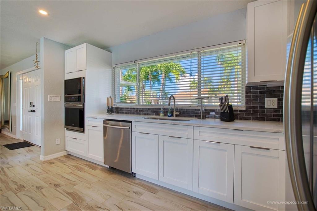 Modern kitchen featuring white shaker cabinetry, stainless steel appliances, a dark subway tile backsplash, and light countertops