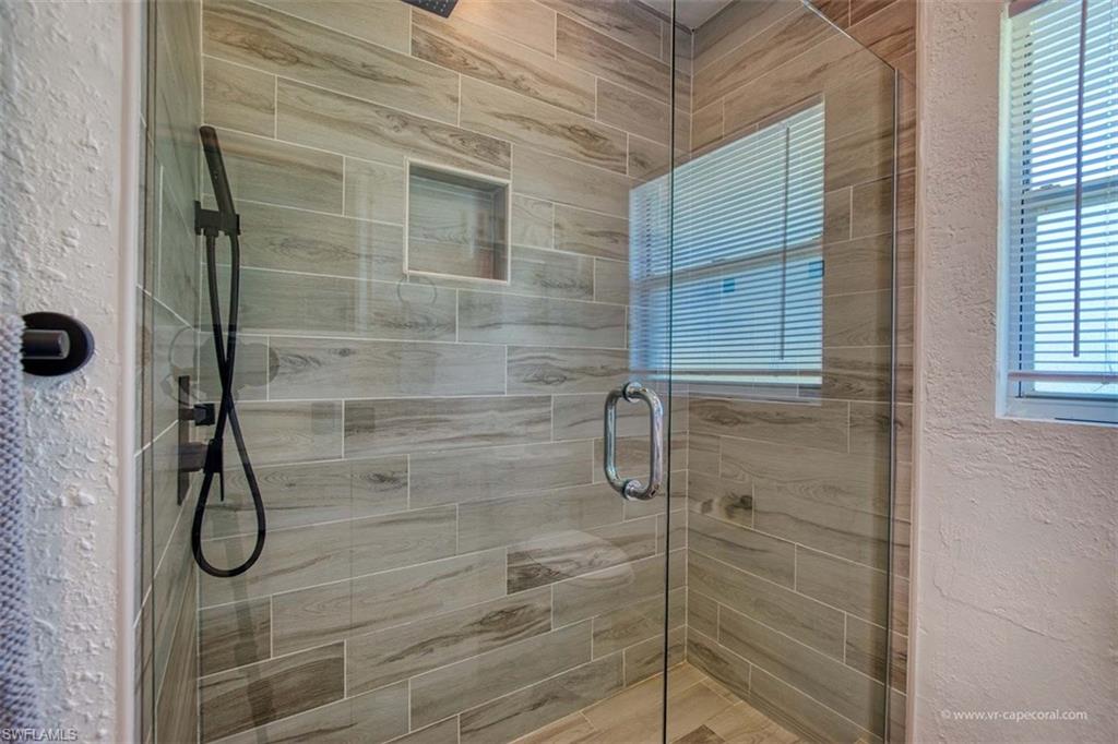 Glass-enclosed shower featuring wood-finish tile walls and flooring