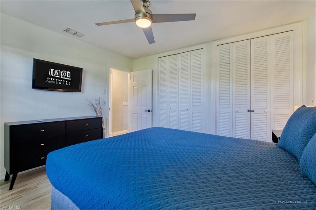 Bedroom featuring light-tone wood-finish flooring, a ceiling fan with integrated lighting, and white louvered bifold closet doors