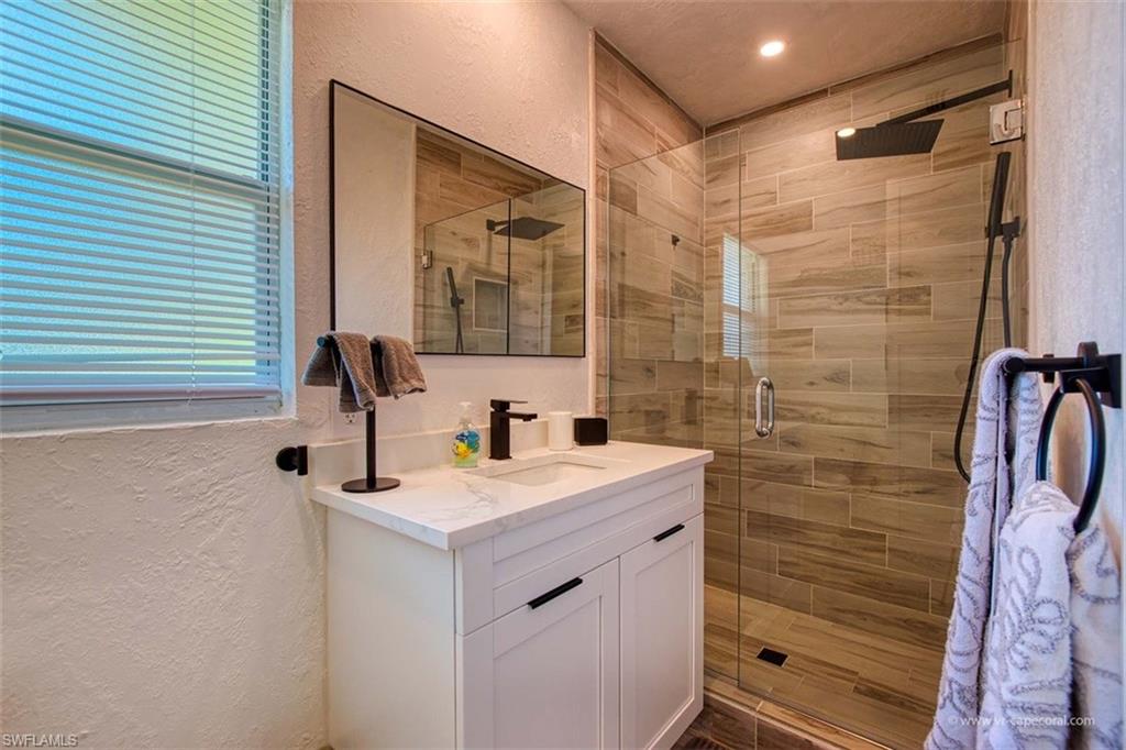 Modern bathroom featuring a glass-enclosed shower with wood-look tile surround and a matte black rainfall showerhead