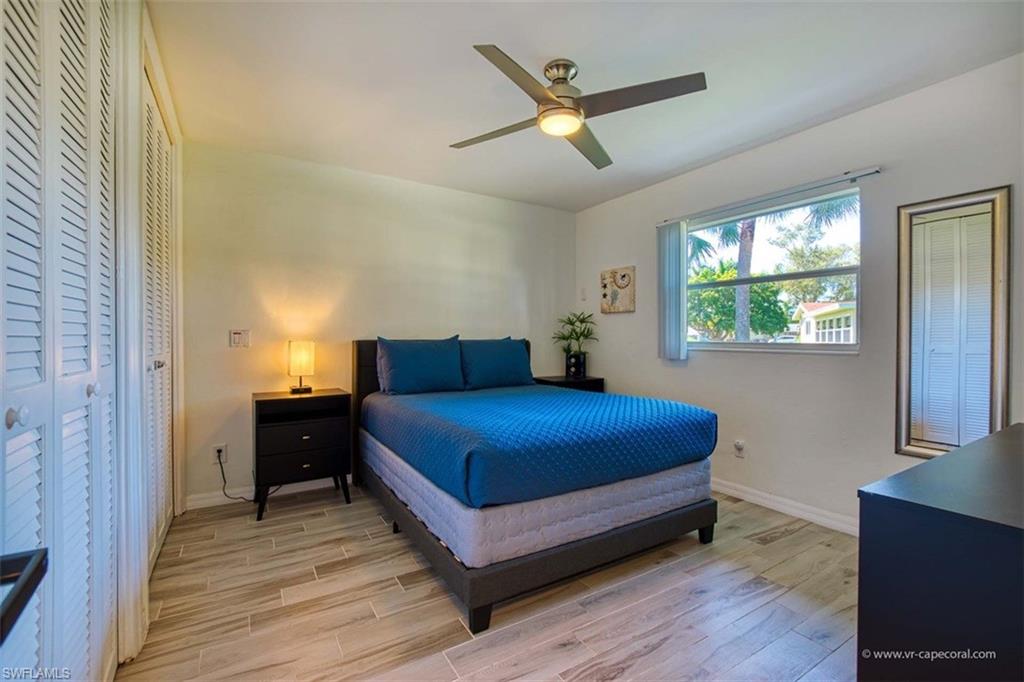 Bedroom featuring wood-finish flooring, louvered bi-fold closet doors, a ceiling fan with integrated lighting, and a window offering exterior views
