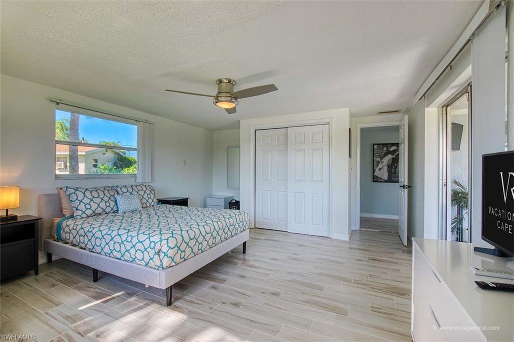 Bedroom featuring light wood-finish flooring, a large window, a ceiling fan with integrated lighting, and a closet with bifold doors