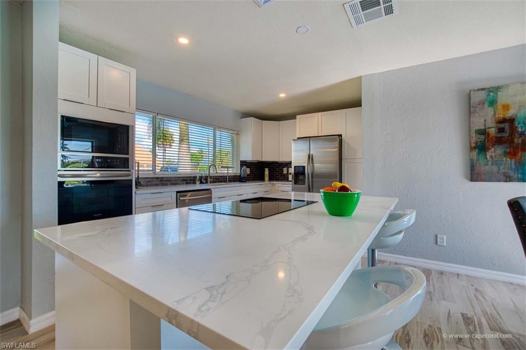 Contemporary kitchen featuring a large island with a smooth cooktop and seating, white cabinetry, stainless steel appliances, and wood-finish flooring