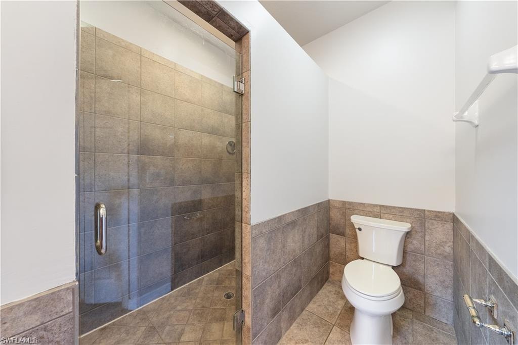 Bathroom featuring tile walls, wainscoting, a shower stall, and tile patterned floors
