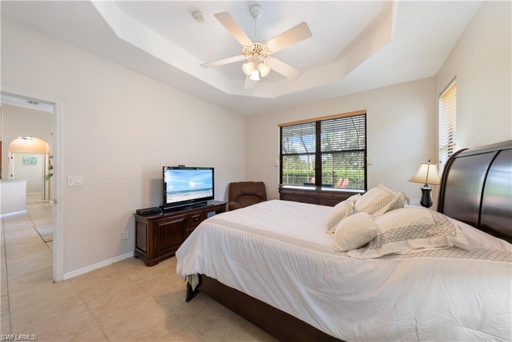 Bedroom with a raised ceiling, arched walkways, a ceiling fan, and light tile patterned floors