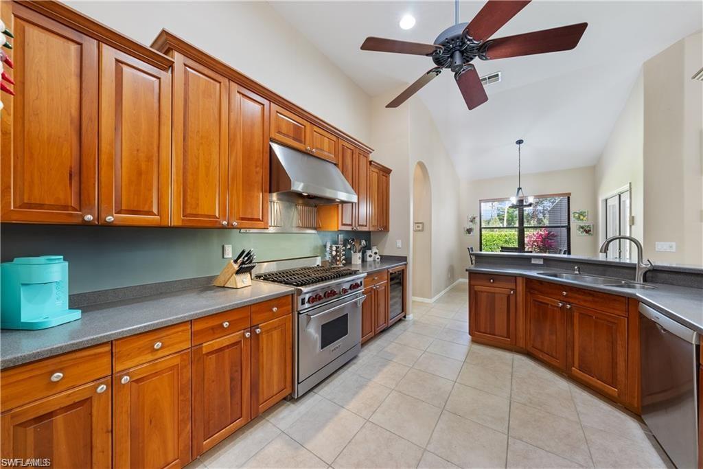 Kitchen with appliances with stainless steel finishes, brown cabinets, under cabinet range hood, vaulted ceiling, and light tile patterned floors
