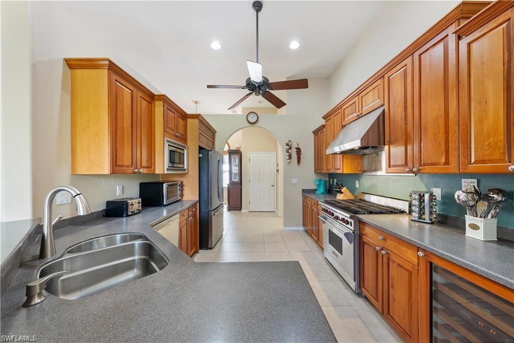 Kitchen featuring brown cabinetry, arched walkways, stainless steel appliances, beverage cooler, and under cabinet range hood